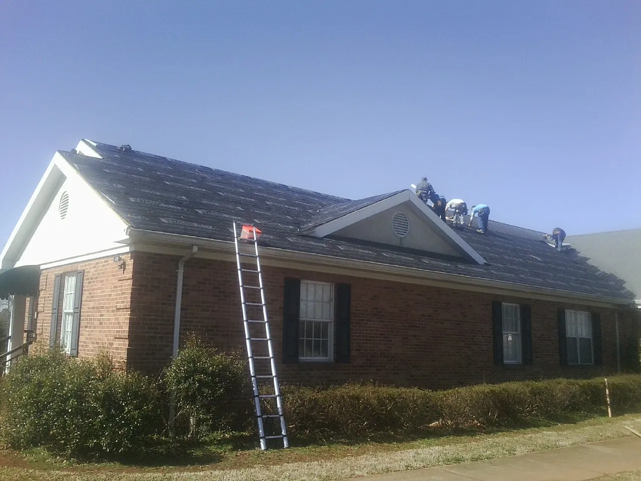 Crew tearing shingles off a brick ranch roof with a ladder set — Emergency Roof Repair work by our crew in La Grande