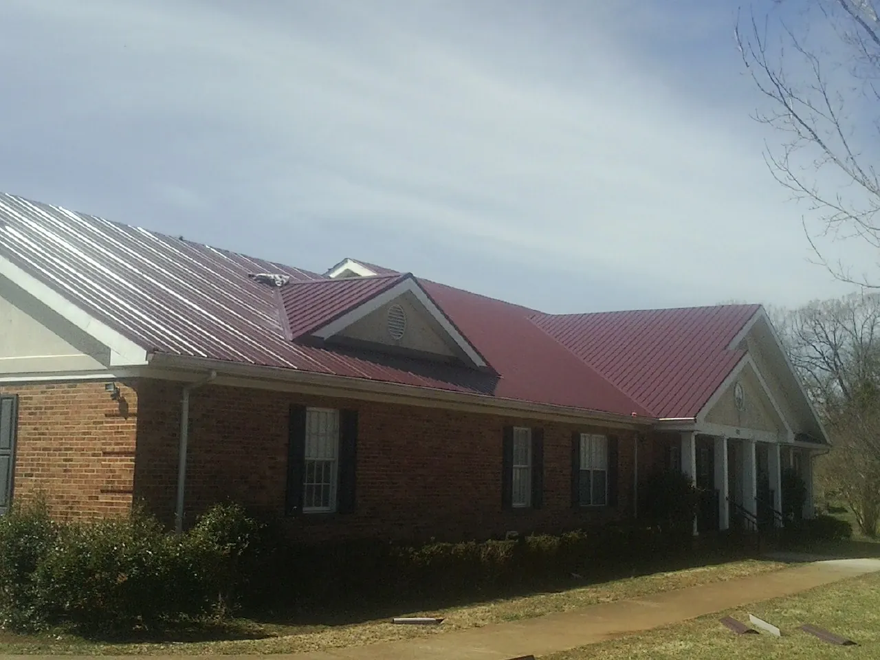 Red metal roof with gabled entries on a long brick building, from a Hail Damage Roof Repair job in La Grande