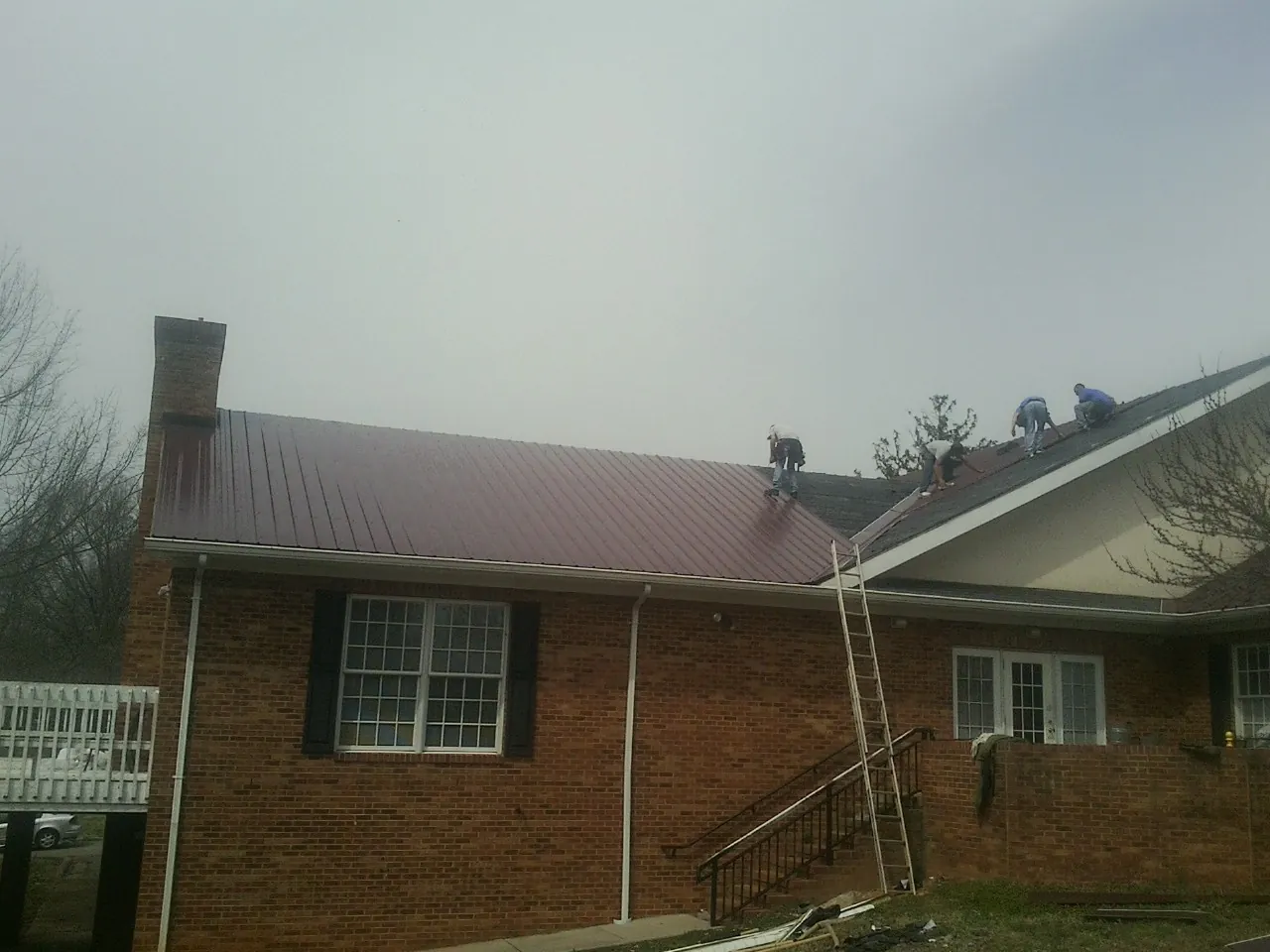 Crew setting red metal roofing panels on a brick home in La Grande
