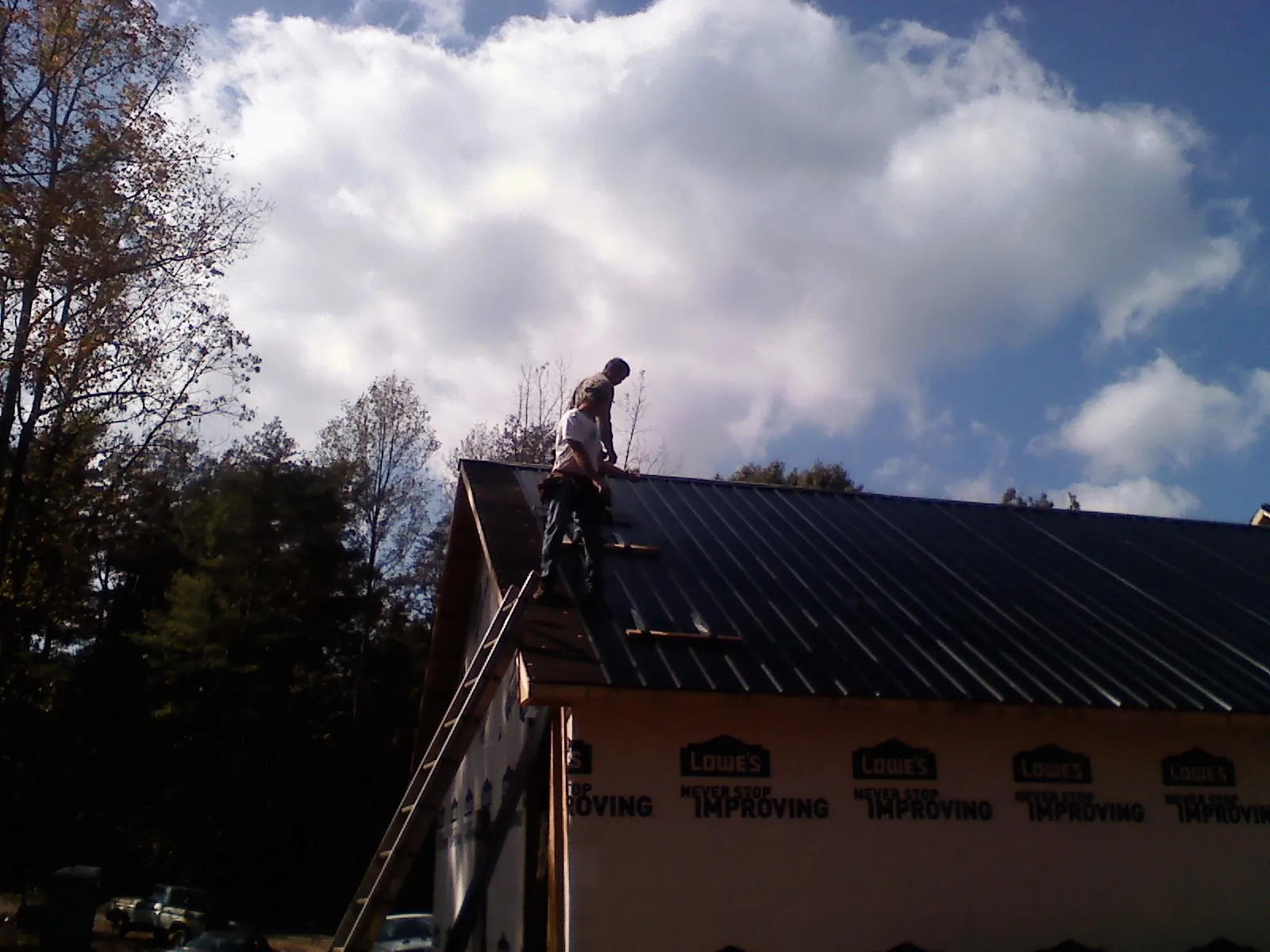Roofer fastening dark metal panels high against a cloudy sky, from a Roof Inspection job in La Grande