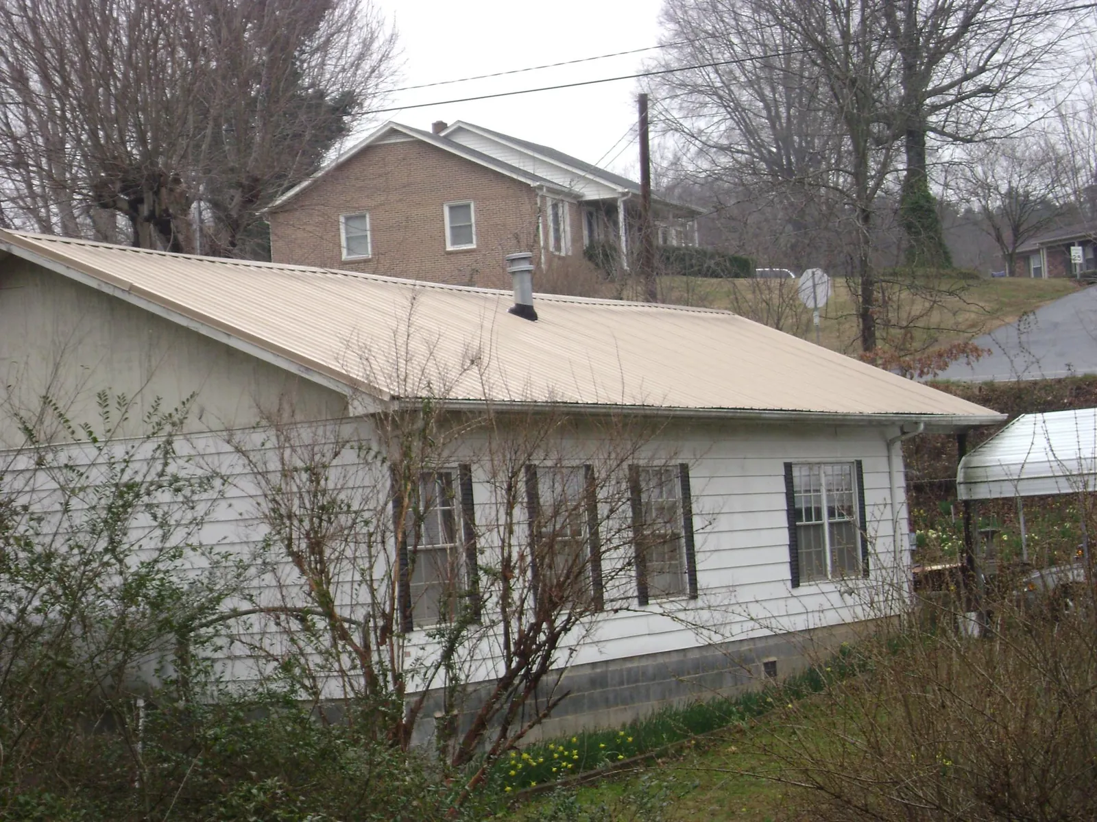 Tan metal roof on a white sided house set into a hillside — Commercial Roofing by Roofing Brothers in La Grande